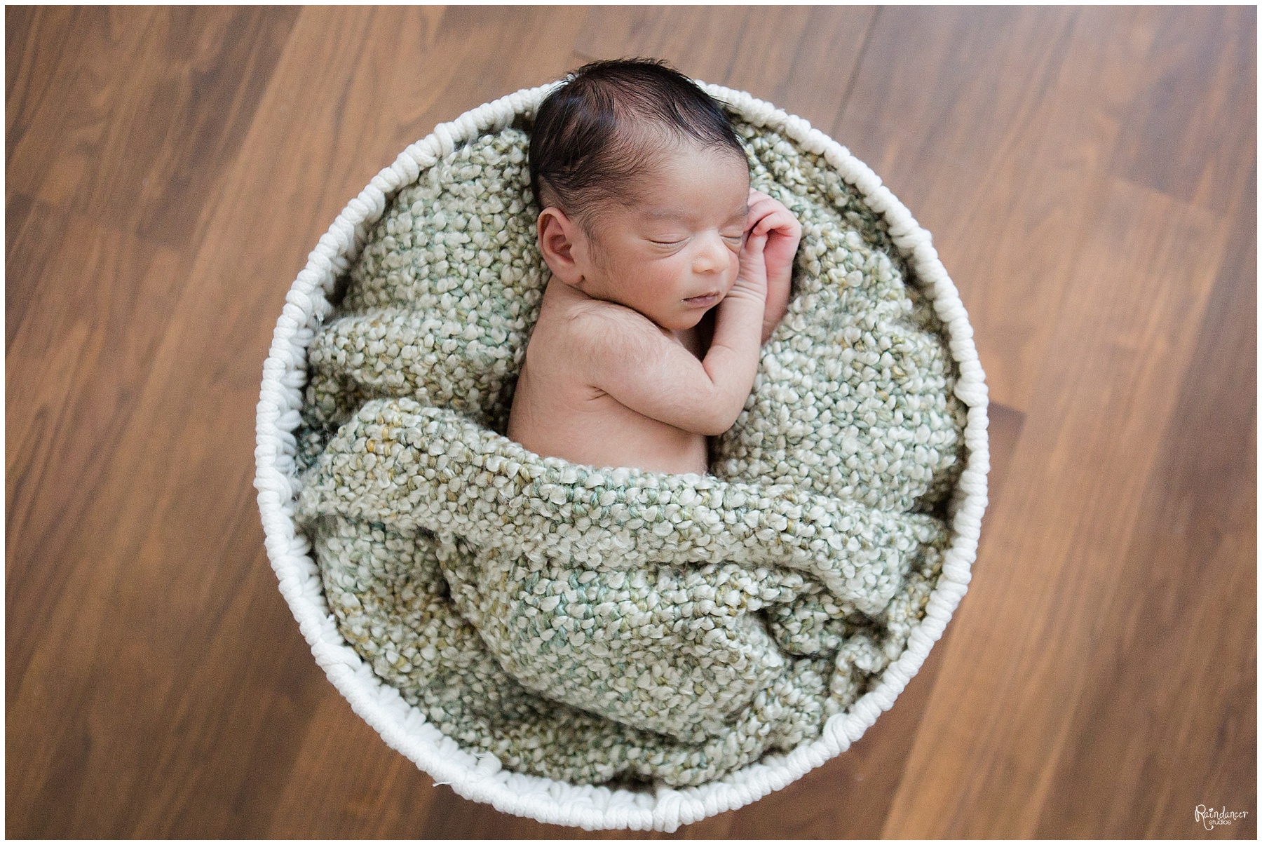Newborn baby boy sleeping with green blanket in white basket by Raindancer Studios Indianapolis Newborn Photographer