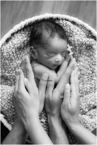 Parents hands on newborn baby boy sleeping in white basket by Raindancer Studios Indianapolis Newborn Photographer Jill Howell